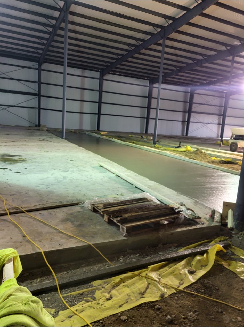 Concrete flatwork underway inside a steel-framed building.
